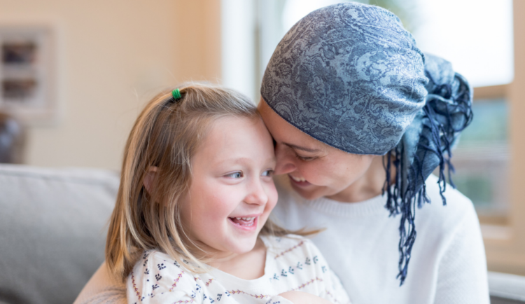 a mom with cancer wearing a headscarf hugs her young daughter