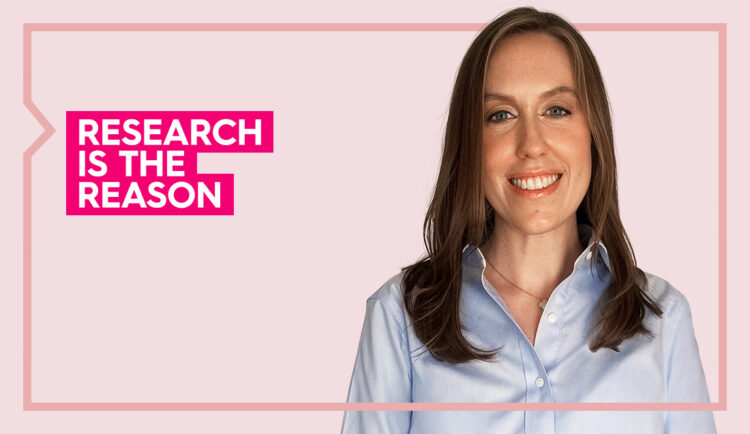 Nicole wears a blue button up shirt and smiles at the camera against a pink background