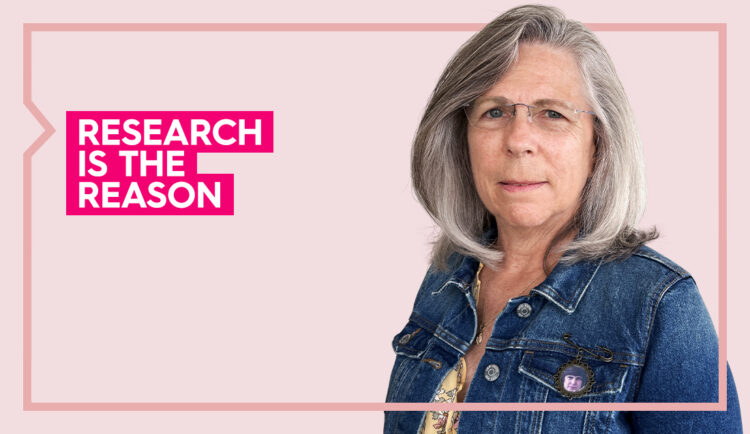 pam wears a blue shirt and smiles at the camera against a light pink background