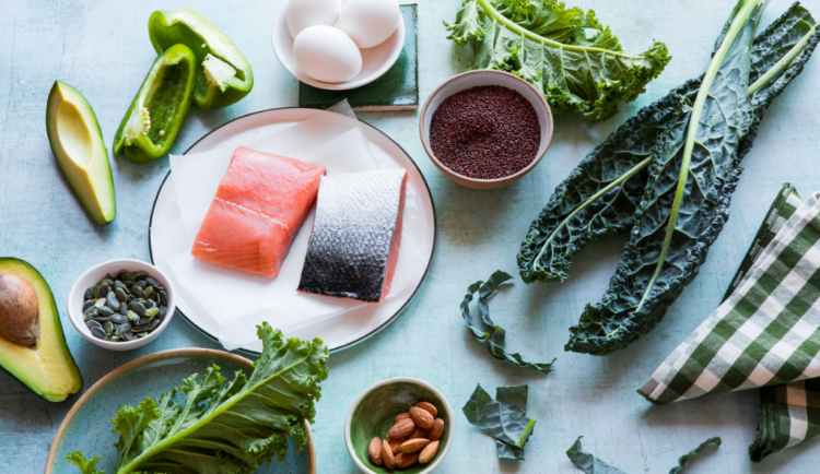 an overhead photo of a mix of healthy foods: salmon, avocado, kale, nuts, eggs, and more