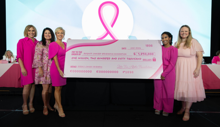 Members of ZTA and BCRF staff hold a check for $1.25 million at ZTA's annual meeting on a stage, all are wearing shades of pink