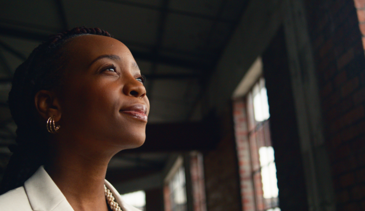 a young black woman looks away from the camera with two windows behind her